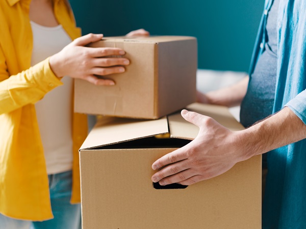 A man and a woman holding and moving cardboard packing boxes as one moves out during their divorce.